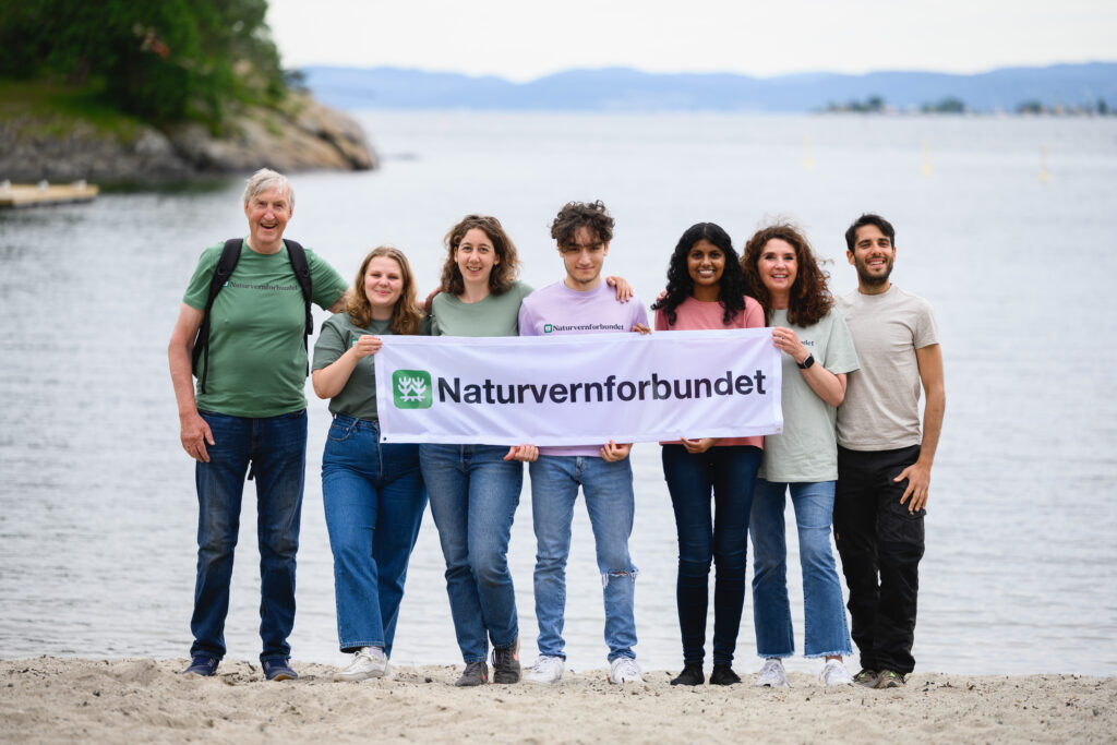 Gruppe mennesker holder opp et skilt av Naturvernforbundet på stranden