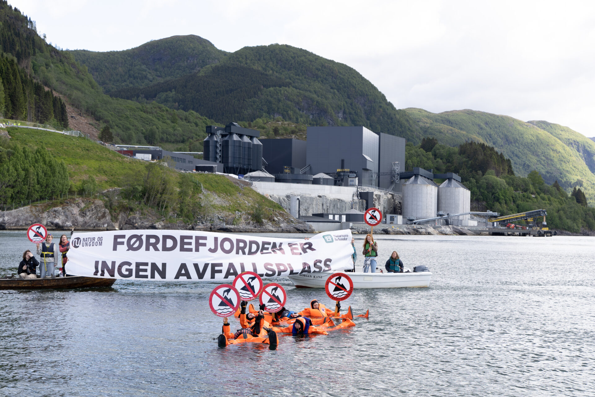Aksjon i Førdefjorden foran Engebøgruven. Aksjonister med håndplakater i vannet og banner mellom to båter.