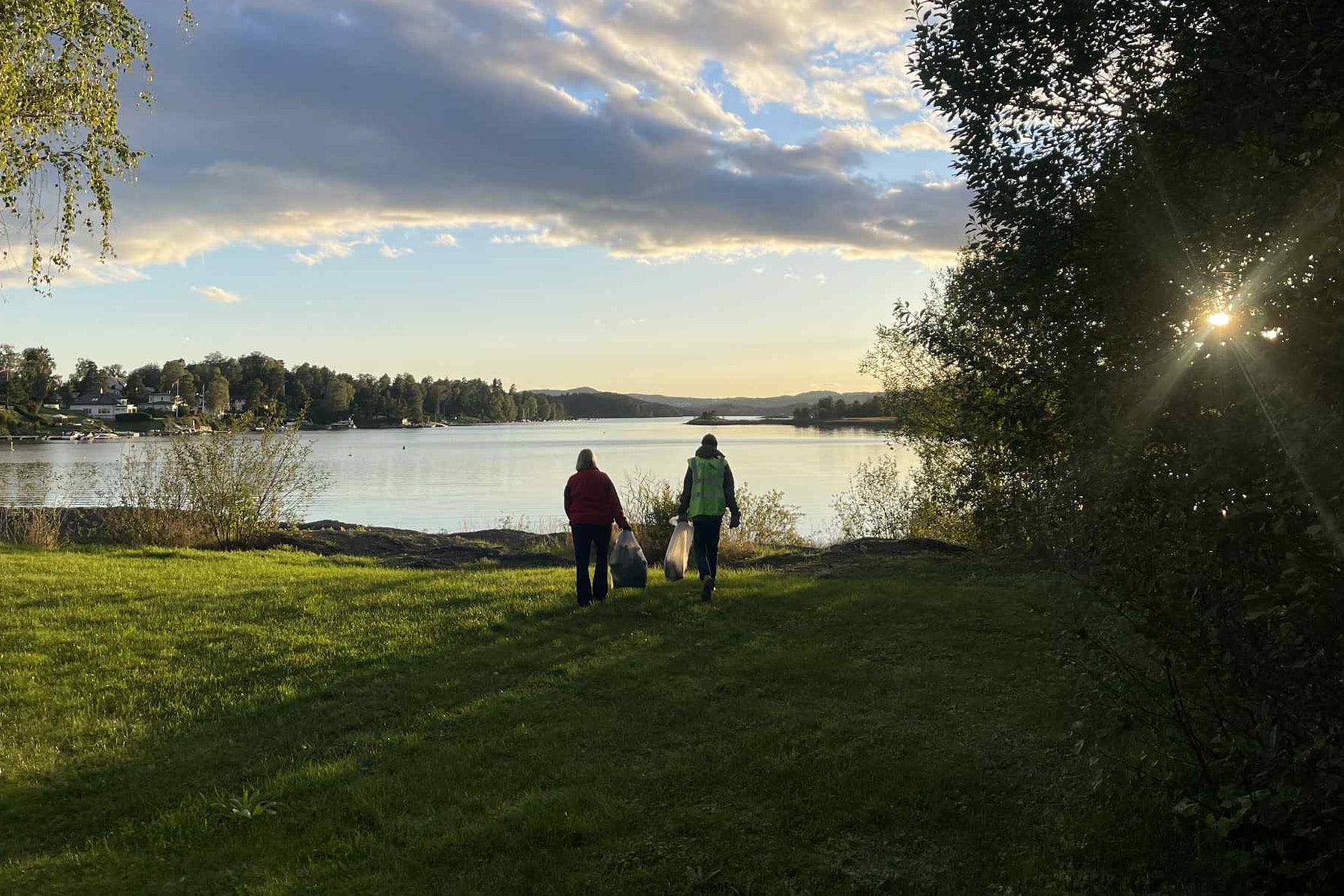 gress, sjø, trær, to mennesker, solnedgang