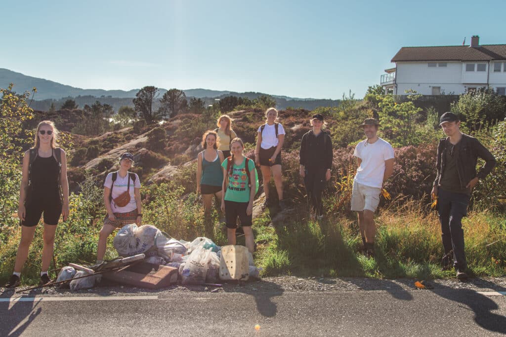 En gruppe mennesker står langs en veikant med søppelet de har ryddet en solfylt sensommerdag
