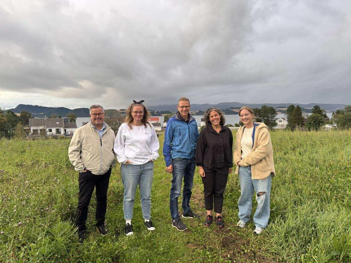 Fem mennesker står på en åker, med en fjord bak seg. De smiler.