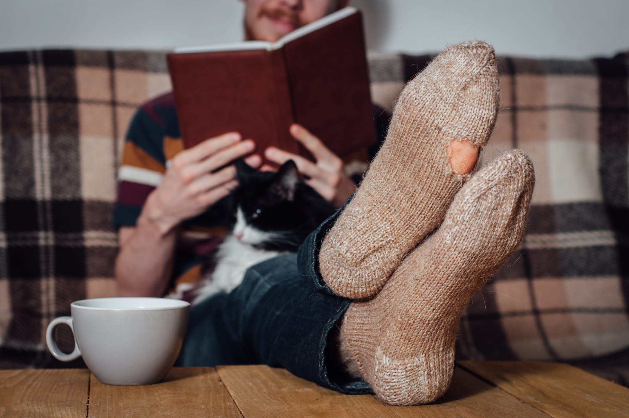 En mann med hull i sokkene som leser bok sammen med katten sin
